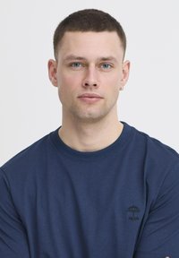 Tengerészkék pamut póló rövid ujjakkal, hímzett esernyő logóval és "re:lax" felirattal a mellrészén. Simító textúra, kerek nyakkivágás.