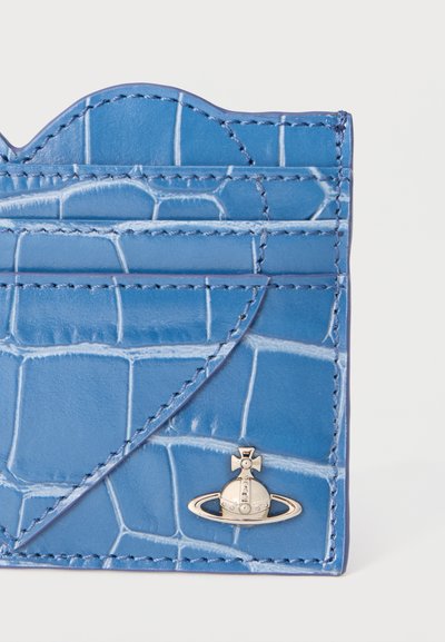 Μπλε δερμάτινο θήκη καρτών με υφή, με πολλαπλές θήκες και ένα μικρό ασημένιο έμβλημα σε σχήμα σφαίρας και σταυρού στην κάτω δεξιά γωνία.