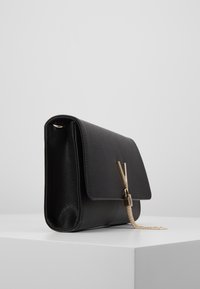 Musta nahkainen clutch-laukku, jossa läppäkotelointi, kullanvärinen ketjutekstuuri ja logokoristeet. Pintahomogeeni tyylikkäällä muotoilulla.