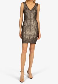 Robe à motif métallique, col en V, coupe ajustée et sans manches. Portée avec des sandales à talons transparentes.