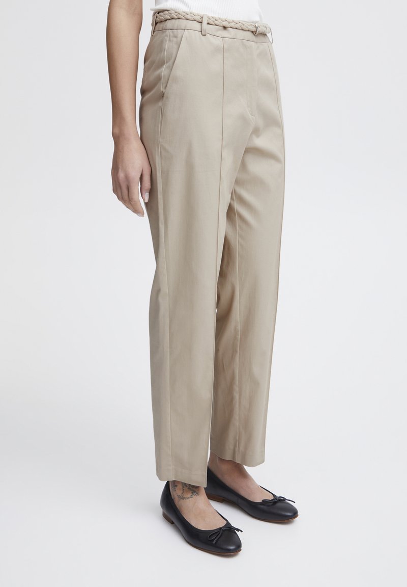 Beige skräddarsydda byxor med flätad bälte, med rak ben-design och sidofickor, som bärs med svarta balettklackar.
