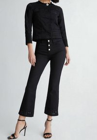 Giacca di jeans nera con dettagli testurizzati, abbinata a jeans neri a vita alta a palazzo con chiusura a bottoni e dettagli con tagli all'orlo.