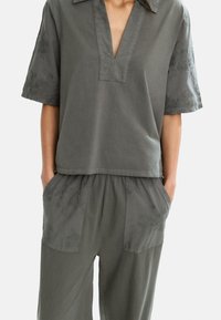Top in cotone grigio con scollatura a V e maniche corte, caratterizzato da ricami floreali. Abbinato a pantaloni morbidi coordinati con tasche e dettagli ricamati.
