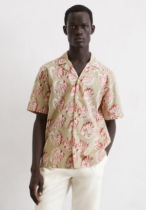 Korte mouwen, lichtgroen shirt met rode tropische bladerenprints. Heeft een gekraagd ontwerp en een knopenfront. Draag het met crèmekleurige broeken.
