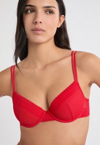 Roter BH mit strukturiertem Design, gezackten Kanten, verstellbaren dünnen Trägern und Bügeln zur Formgebung.