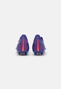 Purple soccer cleats feature a textured mesh upper, contrasting pink accents, and a sleek design with a tapered heel and multiple studs.