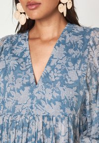 Abito blu a fiori con scollatura a V e vita arricciata. Realizzato in tessuto leggero, presenta una stampa testurizzata e maniche a sbuffo.
