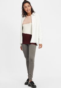 Camisa blanca de manga larga sobre un suéter de punto multicolor con rayas beige, crema y burdeos. Jeans gris ajustados y zapatos negros.