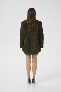 Olivengrüner Wildleder-Blazer, taillierte Form, Ein-Knopf-Verschluss, kombiniert mit einem passenden taillierten Minirock und bordeauxfarbenen High-Heels.