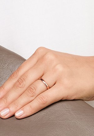 Hand ruht auf brauner Lederoberfläche und trägt einen schlichten roségoldenen Ring am Ringfinger mit natürlichem Nagellack.