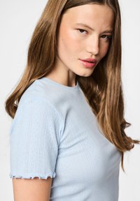 Ανοιχτό μπλε μπλουζάκι κοντομάνικο με υφασμάτινη υφή, με κούφες άκρες στα μανίκια και εφαρμοστή σχεδίαση.