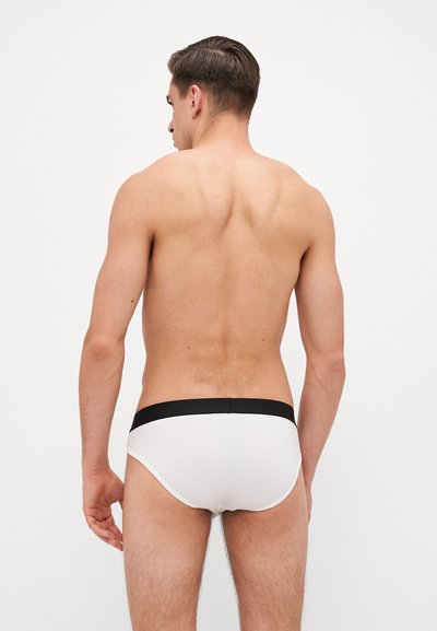Culottes en coton blanc avec une ceinture contrastante noire, conçues pour le confort. La texture semble lisse et ajustée, présentant un style minimaliste.
