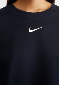 Navy sweatshirt with a ribbed crew neckline and white Nike logo embroidered at the center. Soft, textured fabric, casual design.