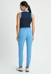 Mörkblå ärmlös polo med blå accenter, i kombination med åtsittande ljusblå byxor, designade med fickor och en slät tygtextur.