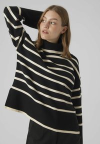 Pull rayé noir et crème avec un col montant, texture côtelée et coupe ample. Coutures d'épaule tombantes et ourlet légèrement asymétrique.