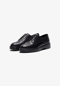 Black leather shoes with a smooth finish, rounded toe, six eyelet lace-up design, and a textured sole for grip. Classic silhouette.