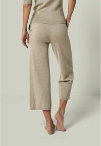 Beige, cropped Hosen aus weichem Strickstoff. Sie haben eine dezente Textur und ein kleines grafisches Design in der Nähe der Gesäßtasche.