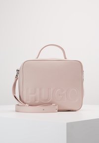 Borsa a tracolla in pelle rosa con logo "HUGO" in rilievo, forma rettangolare, manico superiore e tracolla regolabile. Texture liscia con una trama sottile.