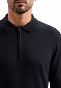 Navy gebreide poloshirt met een zachte textuur, voorzien van een ritssluiting en een klassieke kraag. Strak ontwerp zonder patronen of versieringen.