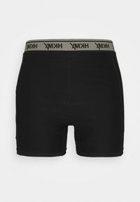 Svarta atletiska shorts med en beige elastisk midjeband som har svart logotyp. Tyget är mjukt med en tajt och figurnära design.