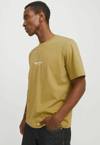 Olive green cotton t-shirt with short sleeves, round neckline, and white text logo on the front. Casual fit, smooth texture.