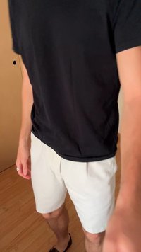 Schwarzes T-Shirt mit kurzen Ärmeln kombiniert mit hellbeigen Shorts. Die Shorts haben vordere Falten, und der Stoff wirkt leicht und glatt.