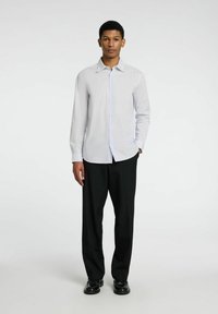 Camisa de botones blanca a rayas con cuello extendido, de mangas largas y pantalones de vestir negros. La camisa tiene un diseño ajustado.