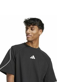 Schwarzes sportliches T-Shirt mit kurzen Ärmeln, mit weißem Adidas-Logo auf der linken Brust und weißem Piping entlang der Schultern.