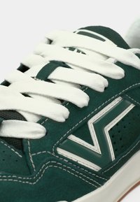 Grüne Wildledersneaker mit weißen Schnürsenkeln, der ein auffälliges Zickzackdesign, perforierte Details und kontrastierendes weißes Nähen aufweist.