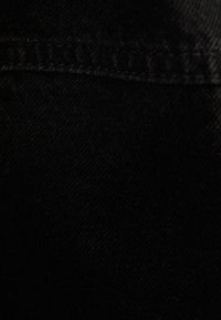 Black denim fabric close-up featuring a smooth texture and visible stitching along the edge, showcasing the material's durability.