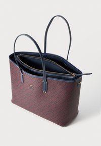 Sac fourre-tout texturé en rouge profond avec un motif géométrique, rehaussé de poignées bleu marine et d'un détail de fermeture éclair doré. Design ouvert montrant des compartiments intérieurs.
