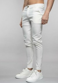 Pantalons slim blancs avec une texture lisse et un léger éclat, dotés d'une fermeture à bouton et de poches latérales, associés à des baskets blanches.