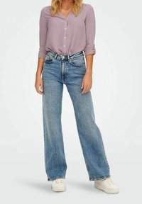 Camicia button-up lilla con maniche arrotolate abbinata a jeans in denim blu a vita alta e gamba larga, con sneaker bianche.