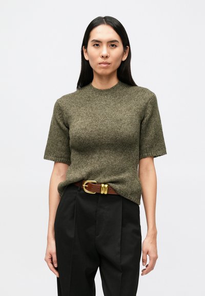 Pull tricoté vert olive à manches courtes avec un col rond, associé à un pantalon noir taille haute et une ceinture marron avec une boucle dorée.