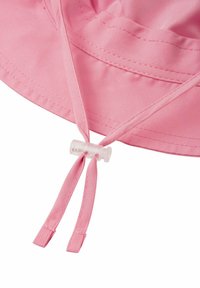 Cappello a secchiello di tessuto rosa con una visiera ampia e due cinturini regolabili. Un toggle in plastica trasparente fissa i cinturini per una vestibilità personalizzabile.