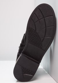 Suela de zapato negra con goma texturizada, que presenta un diseño de banda para tracción. Acabado liso con detalle de cremallera lateral.