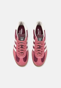 Růžové semišové tenisky s bílými pruhy a texturovanou oblastí šněrování. Klasický design s gumovou podrážkou a značkovou stélkou.