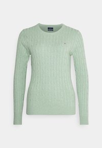 Lichtgroene kabelgebreide trui met een ronde hals, lange mouwen en een klein geborduurd logo op de borst. Zachte textuur.