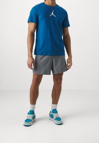 Blå bomullströja med en vit Jordan-logotyp, i kombination med grå shorts och flerfärgade sneakers med teal, lila och grå detaljer.