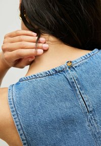 Ärmelloses Denim-Oberteil mit Rundhalsausschnitt, ausgestattet mit einer Knopfverschluss auf der Rückseite und einem leichten Schlitz, akzentuiert durch kontrastierende Nähte.