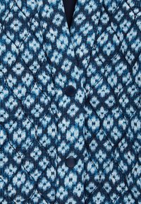 Quiltana jakna v odtenkih modre barve, z cvetličnim vzorcem, diamantnim šivanjem in mornarsko modrimi gumbi. Mehka tekstura s strukturirano obliko.