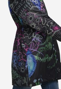Vandafvisende, sort jakke med farverige blomster- og abstrakte mønstre, elastisk talje og lynlås lukning. Letvægts, glat tekstur.