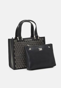 Sort tote taske med cirkulære udskæringer og sølvfarvet hardware.  Indeholder en mindre sort pung med lynlås og præget "SM" logo.