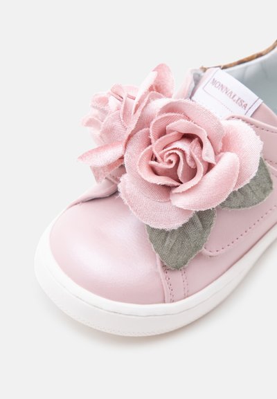 Baskets roses pour enfants avec une grande décoration de rose en tissu et des feuilles vertes sur le dessus près des orteils.