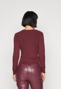 Bordowy prążkowany sweter z długimi rękawami, dopasowanym krojem i lekko zaokrąglonym dekoltem, zestawiony z błyszczącymi bordowymi spodniami.