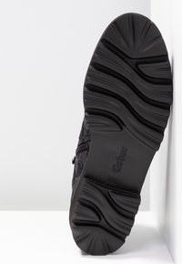 Semelle d'une chaussure noire de la marque Gabor avec des rainures profondes et courbées conçues pour l'adhérence, présentée sur un fond blanc.