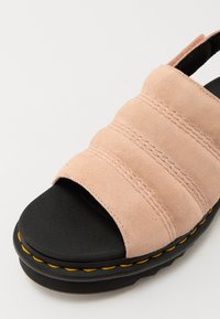 Ružičaste suede klizne sandale s tri horizontalne trake, crnom gumenom potplatom i žutim šavom uz rub. Dizajn otvorenog prsta.