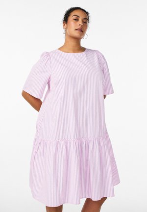 Žena má na sebe voľné ružové šaty po kolená s tenkými zvislými pruhmi a nafúknutými krátkymi rukávmi na bielom pozadí.