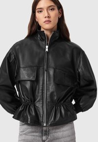 Μαύρο δερμάτινο μπουφάν με ψηλό γιακά, κλείσιμο με φερμουάρ και ελαστική μέση· διαθέτει δύο μπροστινές τσέπες και λεία υφή.