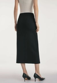 Czarna spódnica do kolan o gładkiej fakturze i dopasowanej talii. Noszona z zielonymi butami na wysokim obcasie, które charakteryzują się minimalistycznym designem.